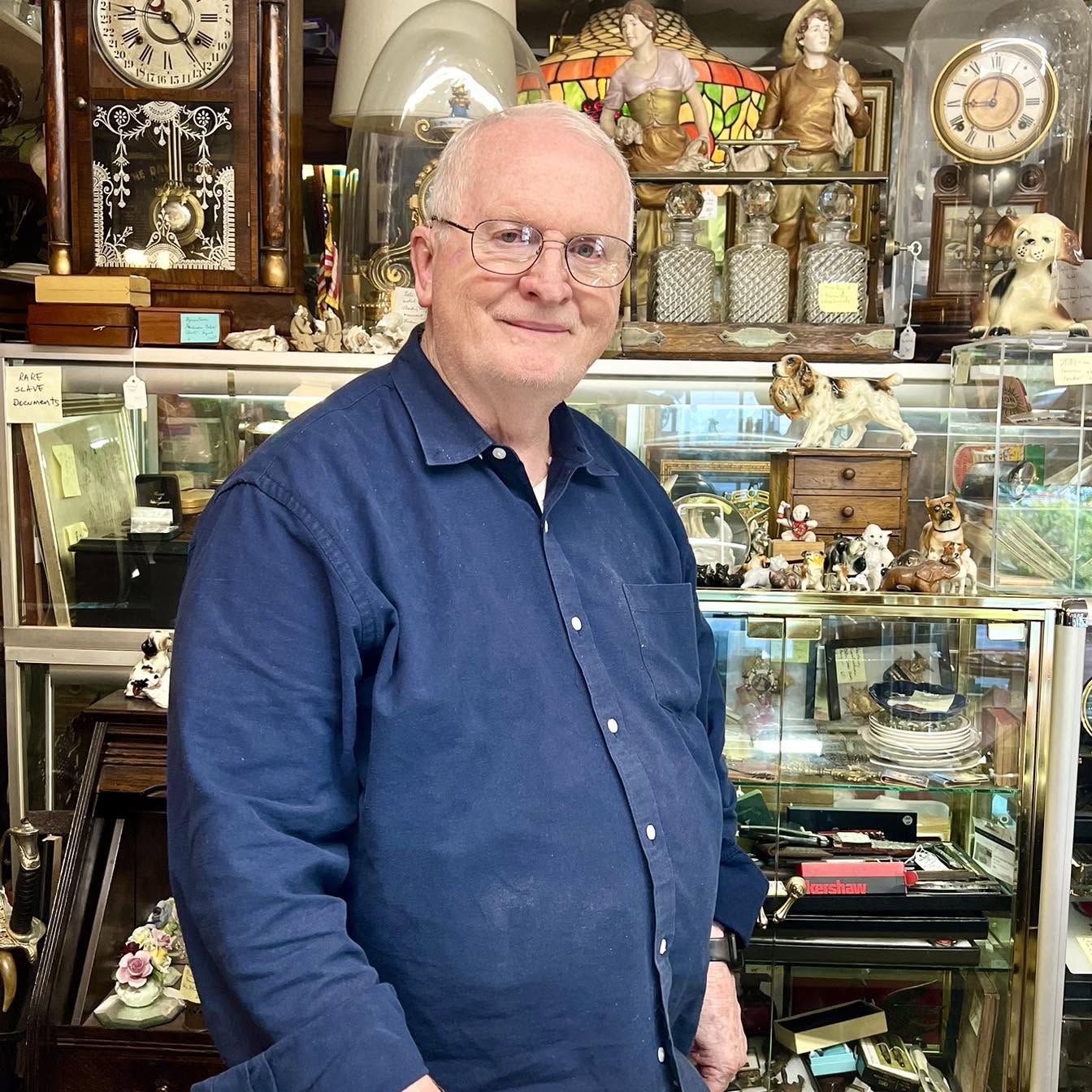 Walter Presswood standing among antique clocks, lamps, and display cases in the store